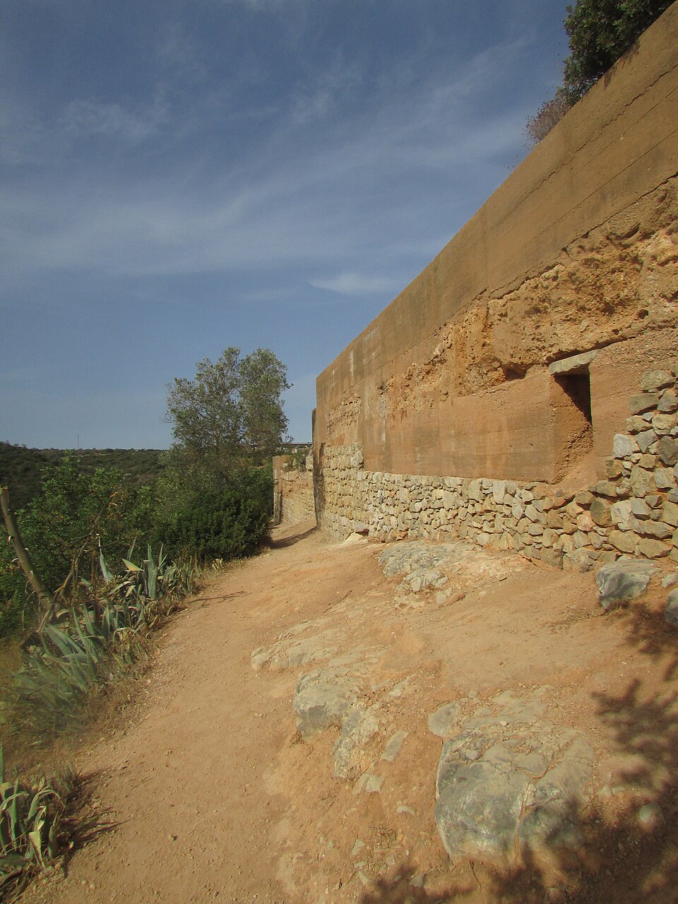 A rammed-earth wall on a stone plinth at Paderne Castle, Portugal. The stone takes the splash and ground damp at the base; the earth above is eroded where its protective coat has gone.