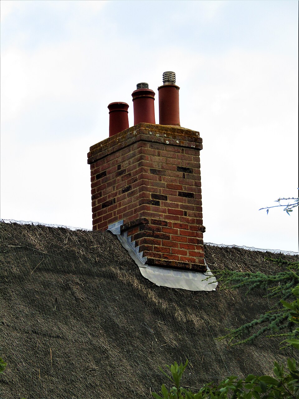 A brick chimney stack rising out of a thatched roof in Mundesley, Norfolk (2022), sealed where it passes through the thatch with lead flashing.