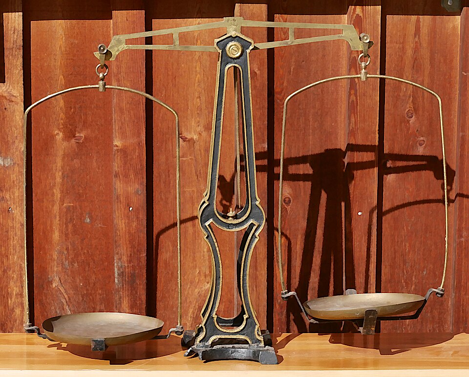 A large equal-arm balance from a German pharmacy, early 20th century: a cast-iron column, a brass beam on a central knife-edge and a pan hung from each end.