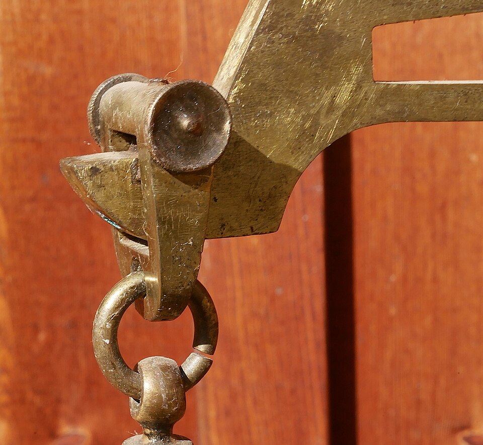The end of the same beam: the pan hangs from a pivot whose position fixes the length of the arm, so a bent or shifted pivot makes the balance false.