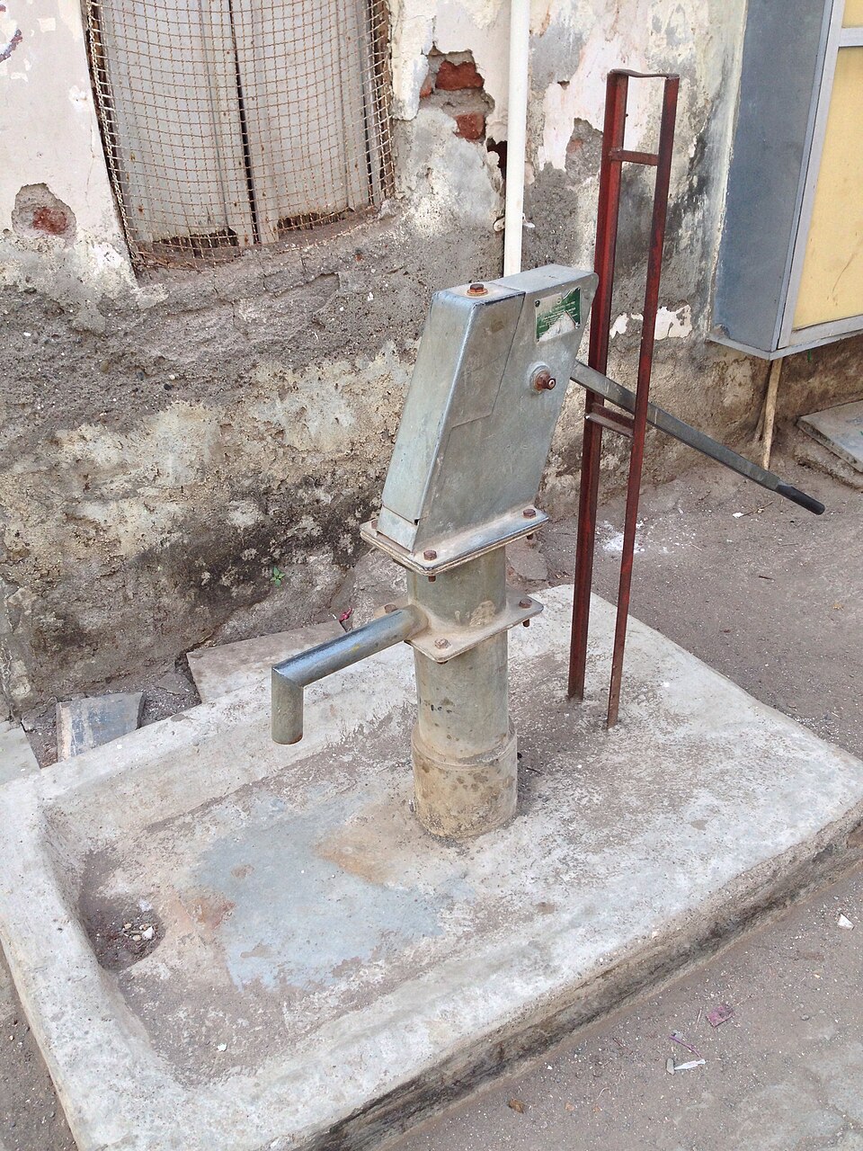 An India Mark II deep-well hand pump on a concrete apron. Its cylinder sits down in the water, so it lifts from well below the 7 m suction limit.