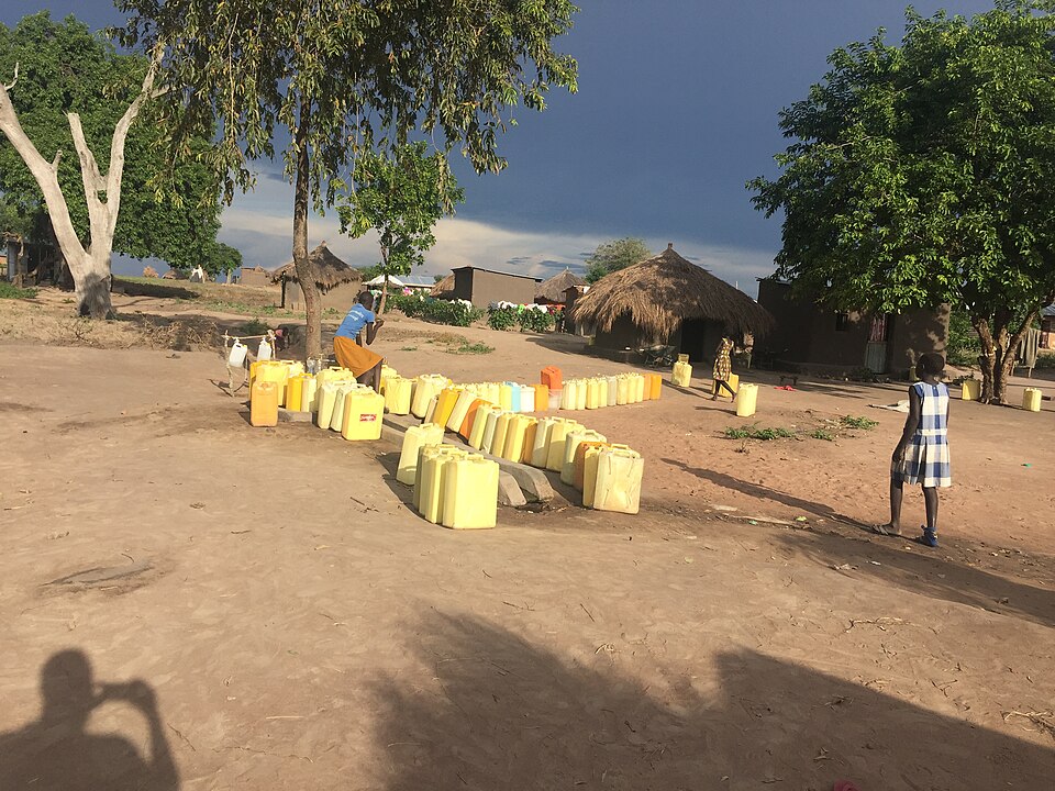 Jerrycans queued at a tap in Rhino Camp, Uganda: the queue is the tap-to-people ratio made visible.
