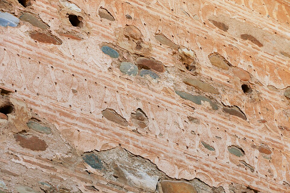 Rammed earth in the walls of the Alhambra: damp subsoil pounded in layers inside formwork. The lines are the lifts, the holes held the form ties — and it has stood eight centuries.
