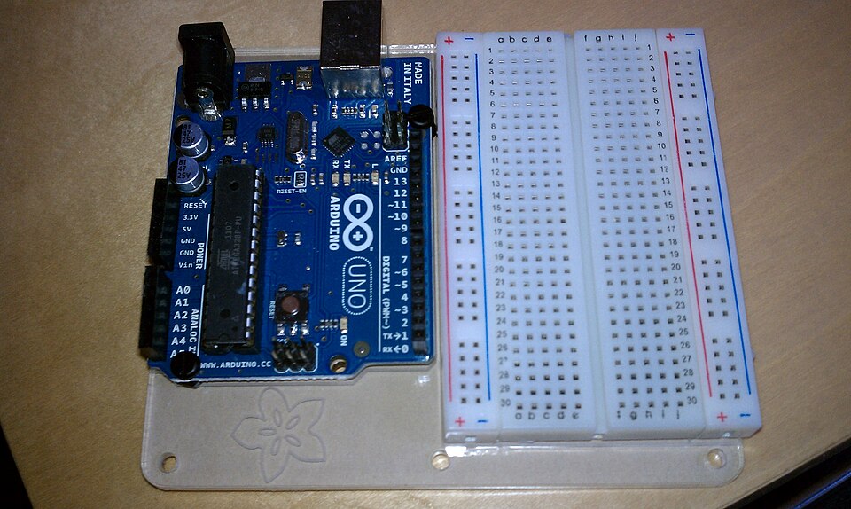 A microcontroller board (Arduino Uno) beside a solderless breadboard. The 28-pin chip on the board holds processor, program memory and RAM: a complete computer that is reprogrammed over USB.