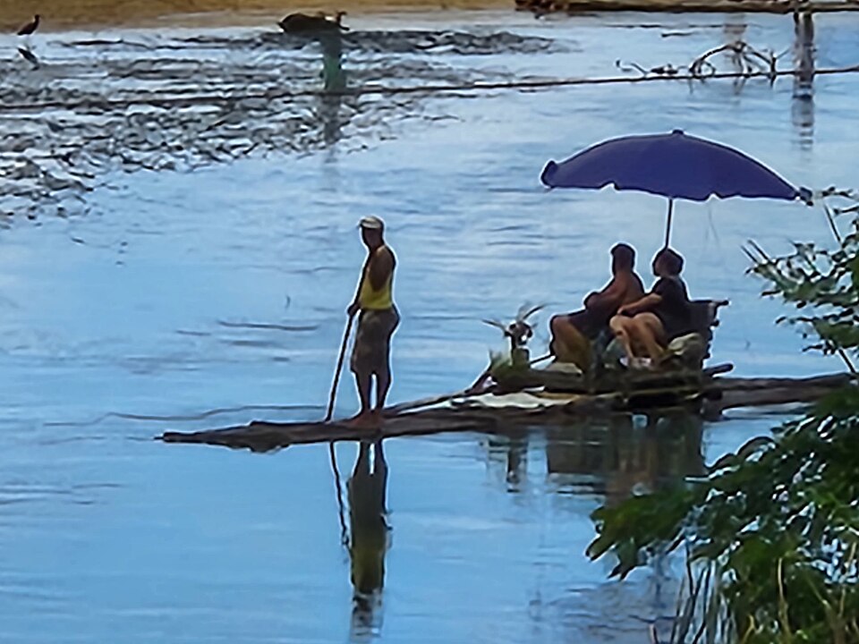 A bamboo raft poled across calm water with passengers seated in the middle, 2022.