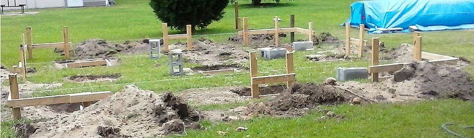 Batter boards on pegs outside each corner of a foundation, with string lines strung between them.