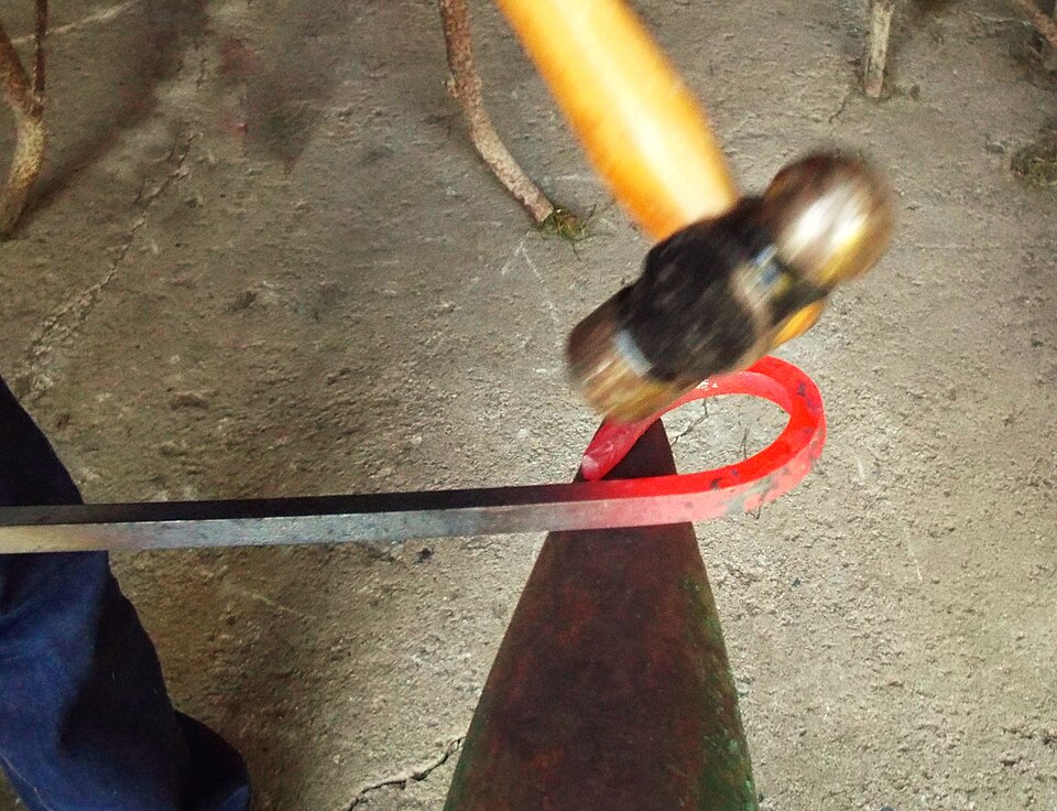 Bending hot steel over the anvil horn at orange heat. The colour is the thermometer: forge above dull red, never below.