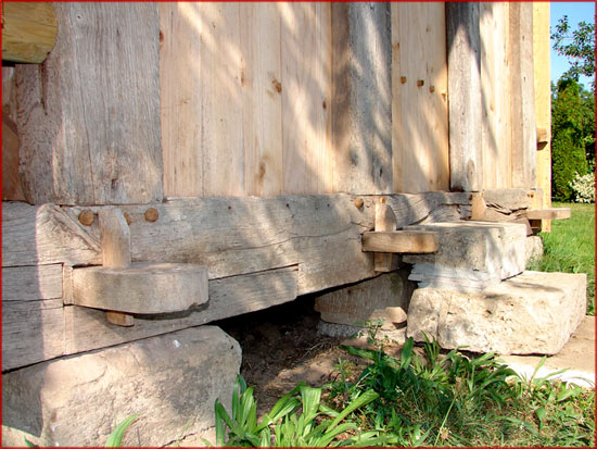 The sill beam of a timber frame resting on stone footings, with tenons pegged into mortises. Stone lifts the timber off the ground, where it would rot.