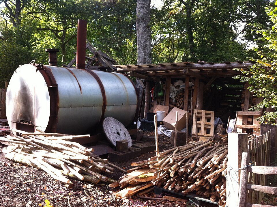 A steel charcoal retort with seasoned billets stacked ready. The wood is sealed inside and heated by burning its own gases, roughly doubling the yield of an earth clamp.