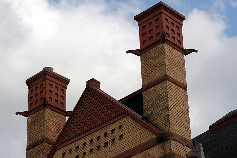 Brick chimney stacks rising well clear of the ridge and the gable, with terracotta pots on top. Height above the roof is what keeps wind from pushing smoke back down.