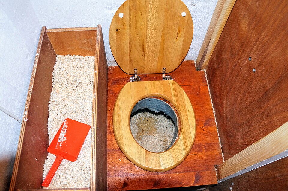Inside a sawdust latrine — seat, chute, and the bin of cover material that makes the system work.