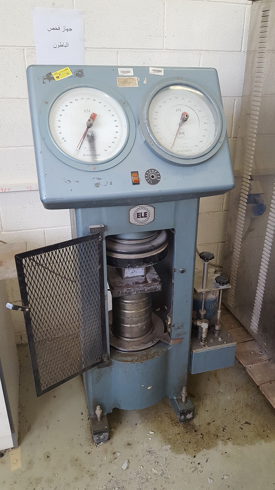 A compression testing machine (2016): a cube is crushed between its platens and the dials record the load at failure.