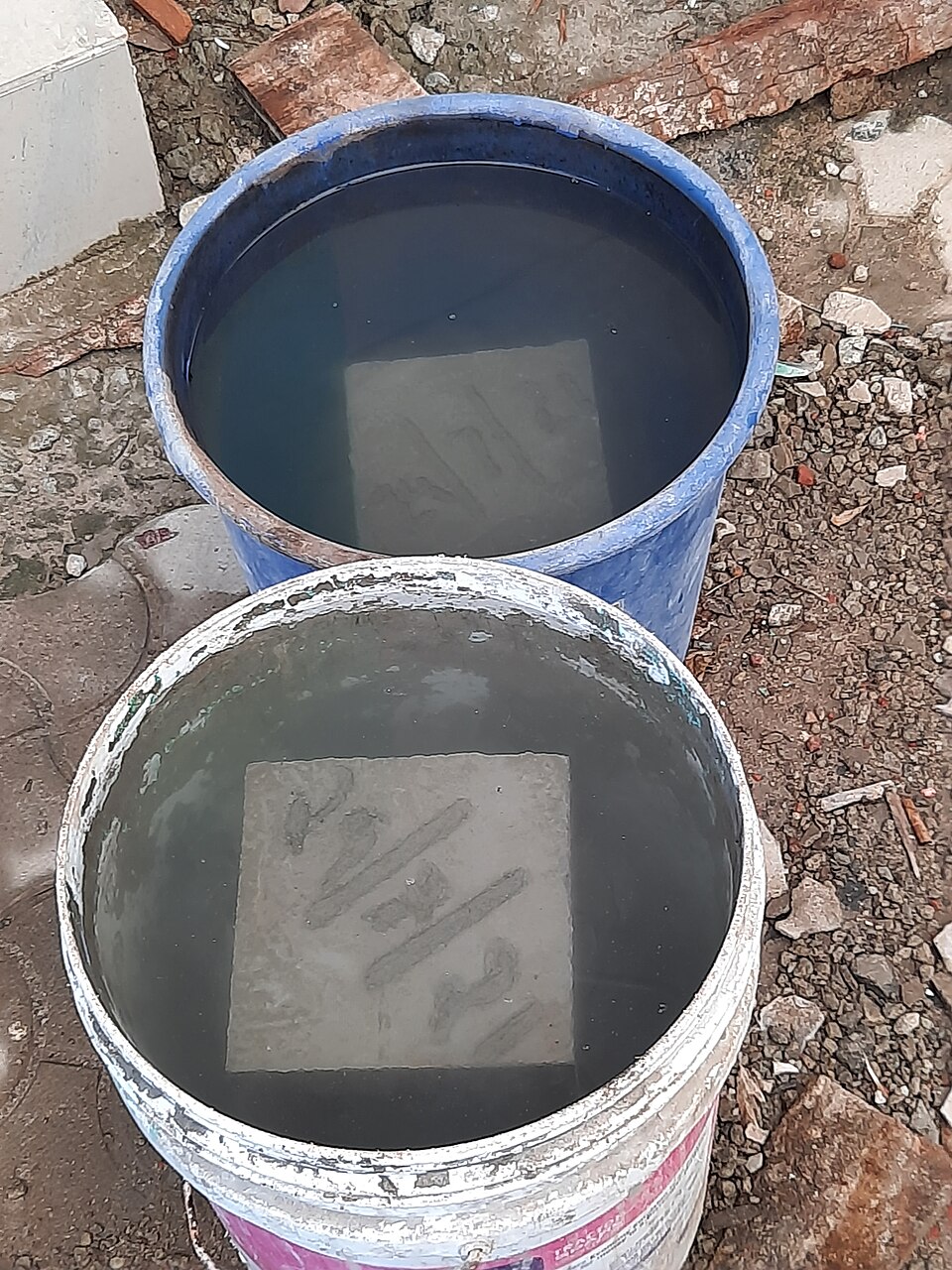 Concrete test cubes curing under water in buckets (2021), kept wet until they are crushed at 7 and 28 days.