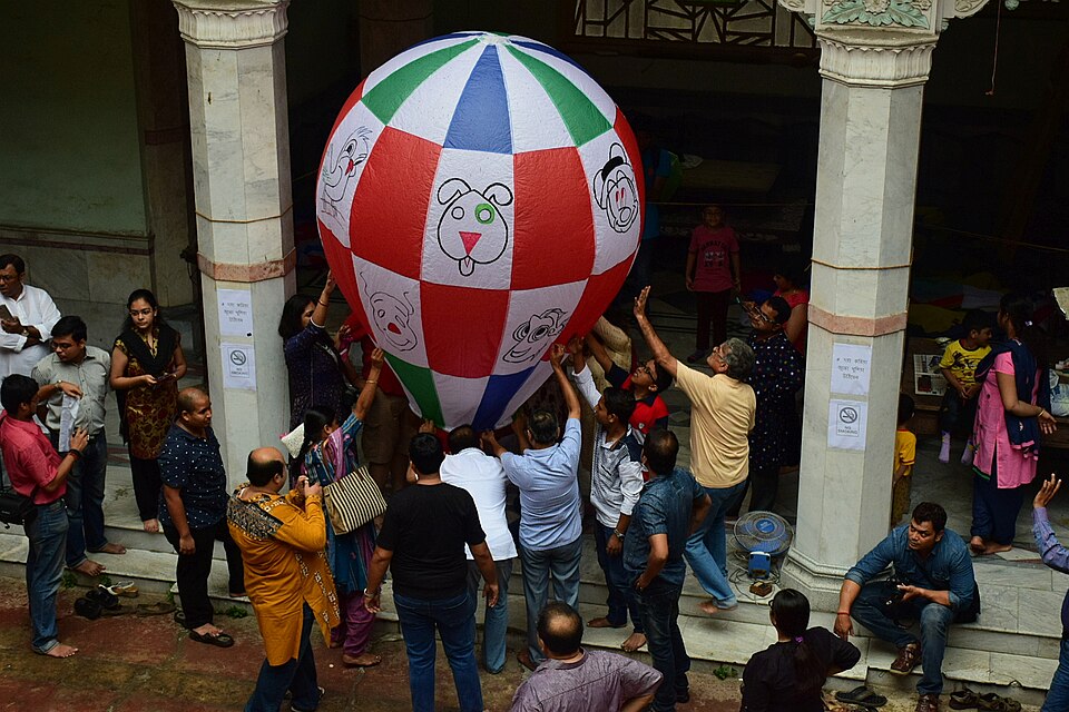 A large paper balloon being filled and held by many hands at an event in Kolkata, 2017.