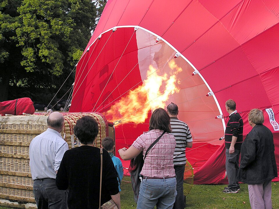 A burner driving hot air into the open mouth of a hot-air balloon lying on its side, before it stands up.