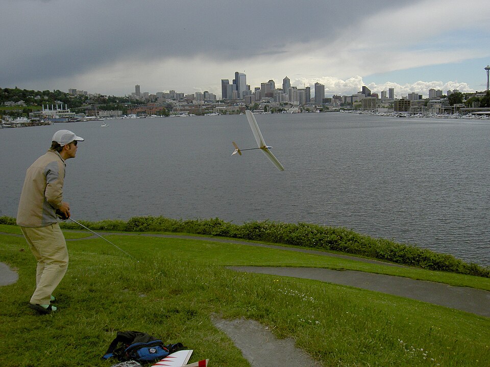 A hand-launched model glider a moment after the throw, climbing out over water.