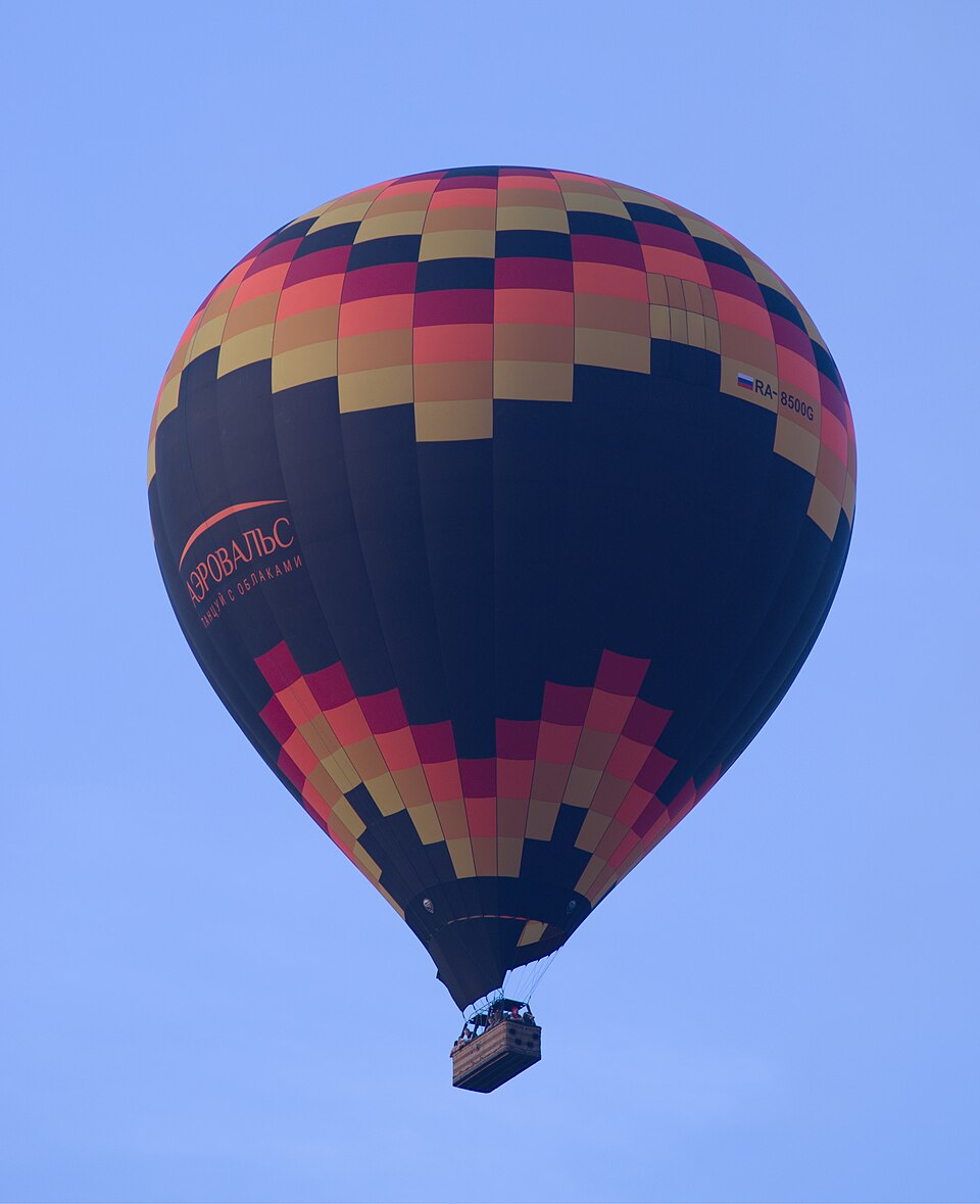 A hot-air balloon in flight, 2021: the basket hangs below the open mouth, the burner between them.