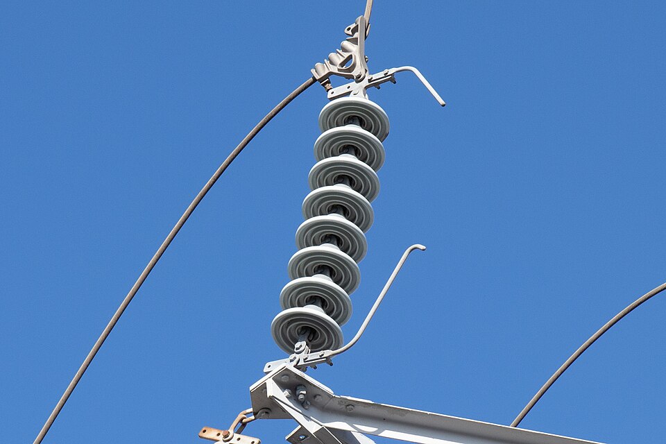 A string of disc insulators holding a 66 kV conductor in Japan. Higher voltage needs a longer string: each disc adds distance a current would have to jump across the surface.