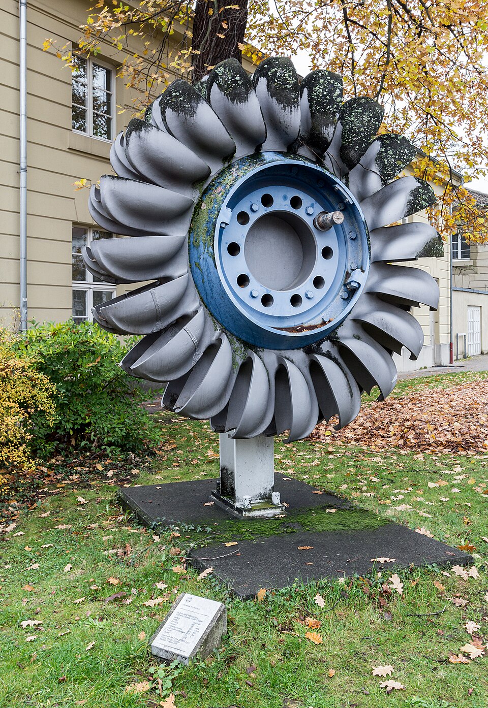 A Pelton turbine runner on display in Karlsruhe: a ring of split, cup-shaped buckets struck by a high-speed water jet. Pelton wheels suit high heads and small flows, which makes them the usual choice for mountain micro-hydro.