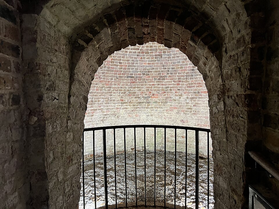 Inside the ice well of the ice house at Kew Gardens: a brick-lined pit reached through a narrow passage. Winter ice was packed here in straw; the small opening and the mass of ground around the pit are what kept it through summer.