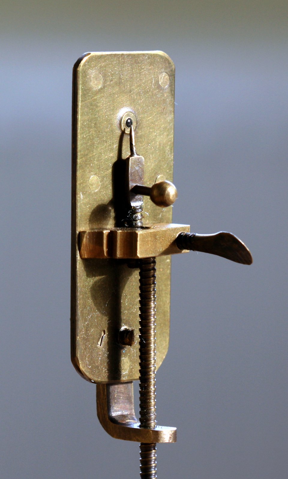 A replica of a Leeuwenhoek microscope, about 5 cm tall: the tiny glass lens sits in the hole at the top of the brass plate, the specimen goes on the point just behind it, and the screws move the point to focus. The eye goes right up against the plate.