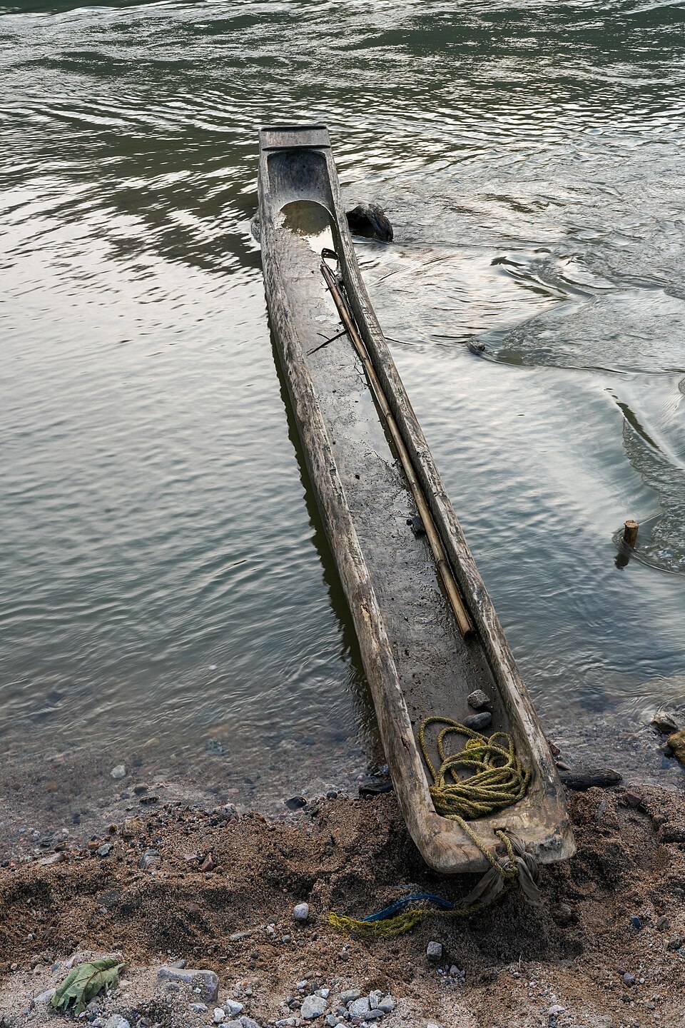A dugout on the Simsang river, Meghalaya: one log, hollowed, with a bamboo pole for pushing off the bottom. Long and narrow runs fast and straight but tips easily — a boat for calm river water.