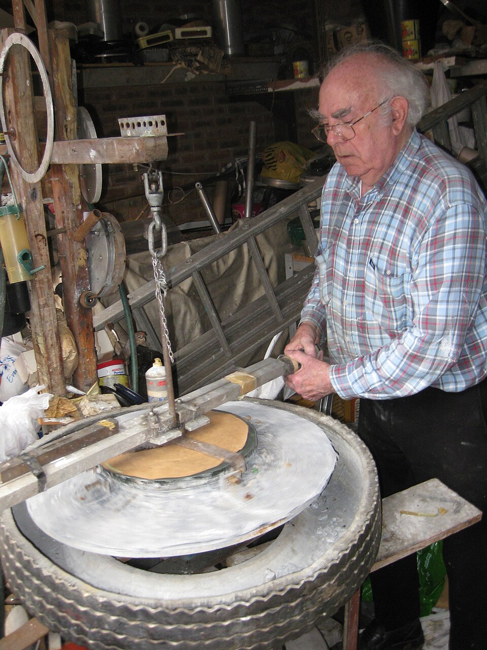 Grinding a large optical disc by hand on a turntable: the tool turns with abrasive and water while the maker strokes across it. Small lenses are ground the same way in a tool cut to the curve wanted.