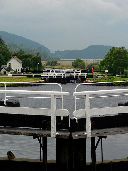 A flight of locks at Dunardry on the Crinan Canal, seen over the balance beams of one pair of gates to the next lock up. Each chamber lifts a boat a few metres; a flight climbs a hill in steps.