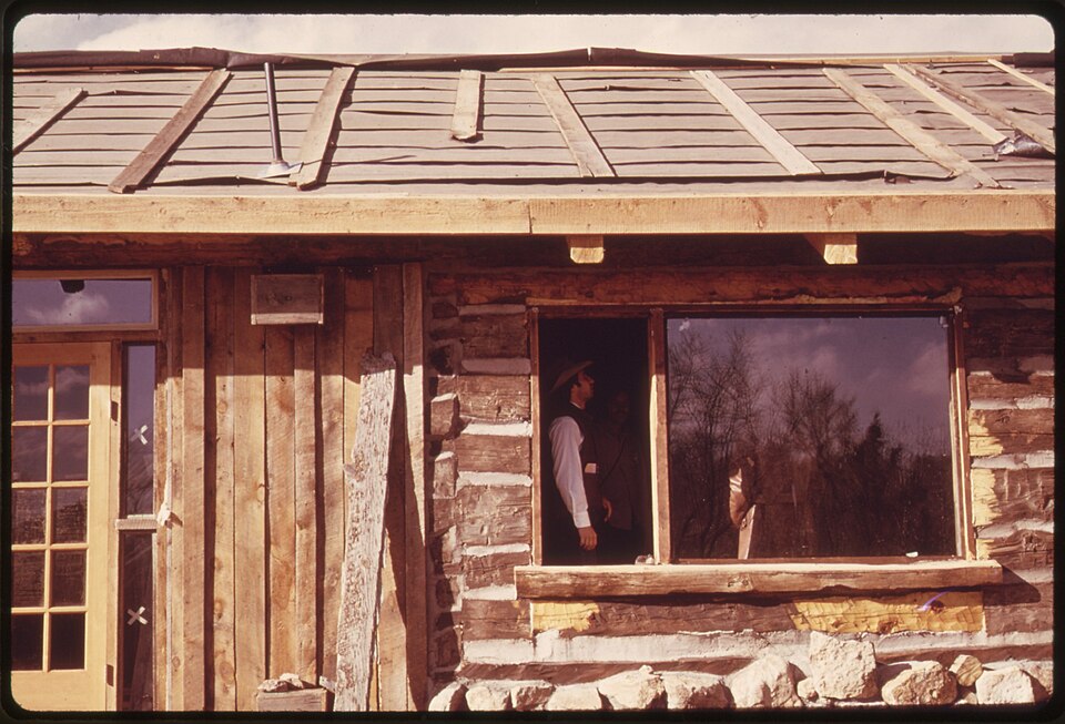 A log wall under construction, 1974: chinking and daub between the logs, and a window frame set into the wall with room above it for the logs to settle.