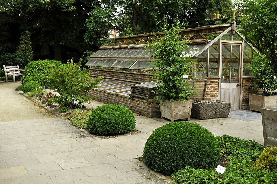 A small glasshouse on a brick base with a row of cold frames in front of it, in the botanic garden at Leuven, Belgium.