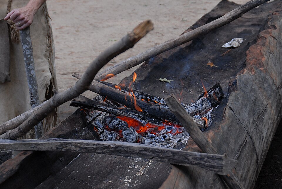 Hollowing a dugout with fire (US National Park Service): a small fire burns along the log, and the charcoal is scraped out between burns.
