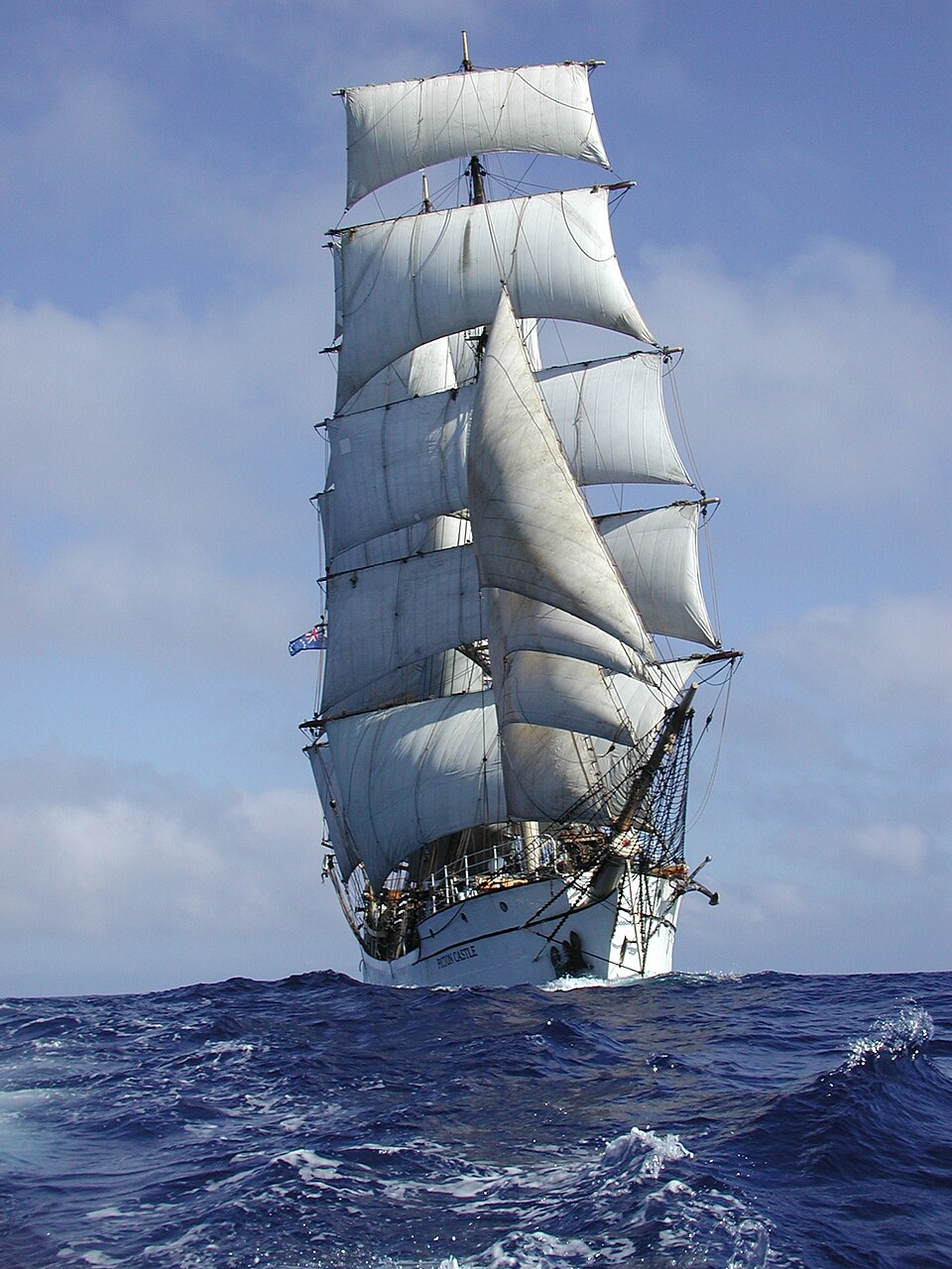 The barque Picton Castle under full sail: square sails on its masts, and fore-and-aft sails between them.