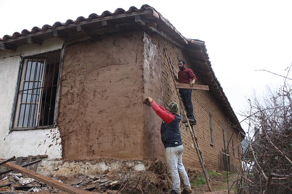 Re-plastering adobe walls with mud after the 2010 earthquake in Chile. The same soil as the blocks, applied in coats onto the damped wall; note the eaves overhang that keeps the new plaster dry.