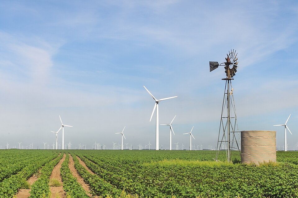 Roscoe Wind Farm, Texas: electricity-generating turbines beyond an old multi-blade farm windmill that pumps water — the same wind used two ways, a century apart.