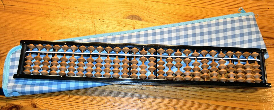 A Japanese soroban: one bead above the bar worth five and four below worth one, one column per digit. Addition and subtraction are done by moving beads, with the carries by hand.