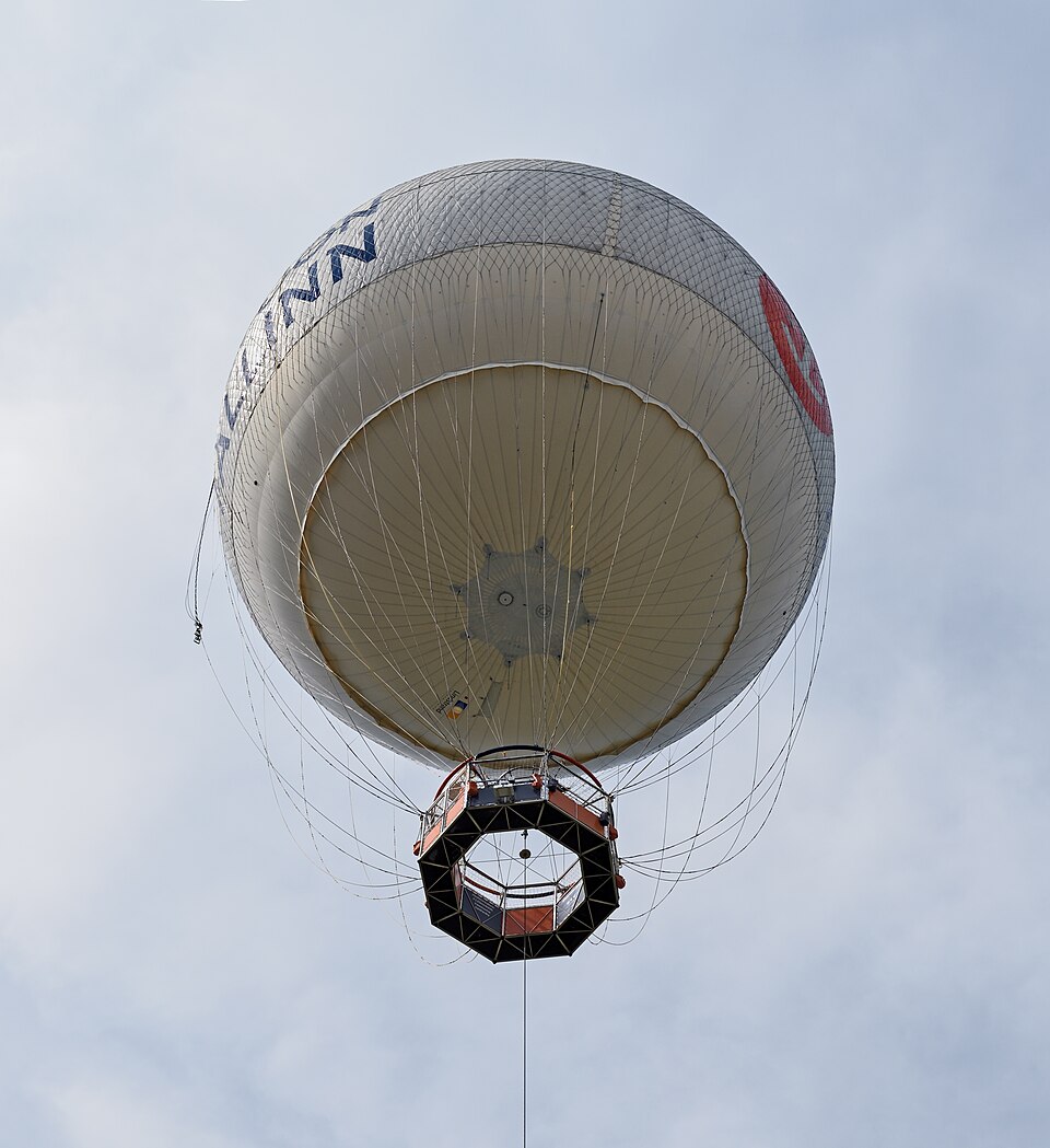 A tethered passenger balloon over Tallinn, 2015, from below: the gondola hangs from a net over the envelope, held by one cable to a winch.