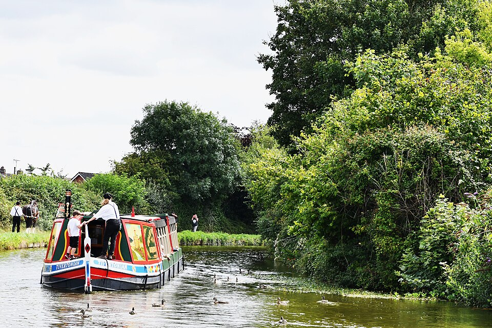 A horse-drawn barge on the Grand Western Canal, Tiverton — the horse walks the towpath at left. On still water one horse can move a load that would take more than ten horses and carts on a road.