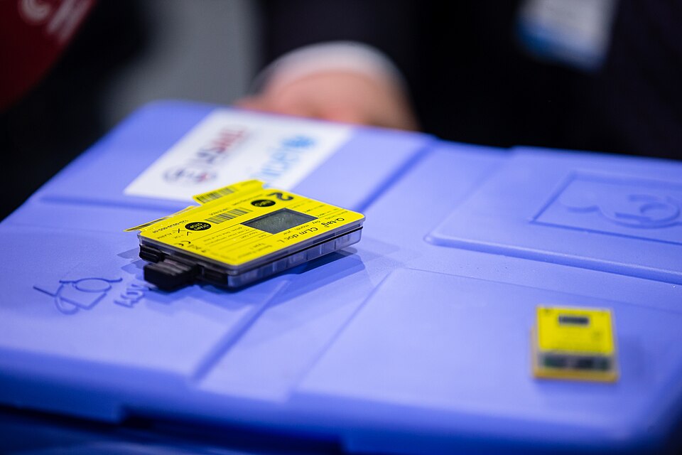 A vaccine carrier with electronic temperature loggers on the lid (Ukraine, 2021). A logger records every temperature the vaccine saw in transit, including a freeze that a thermometer read twice a day would miss.
