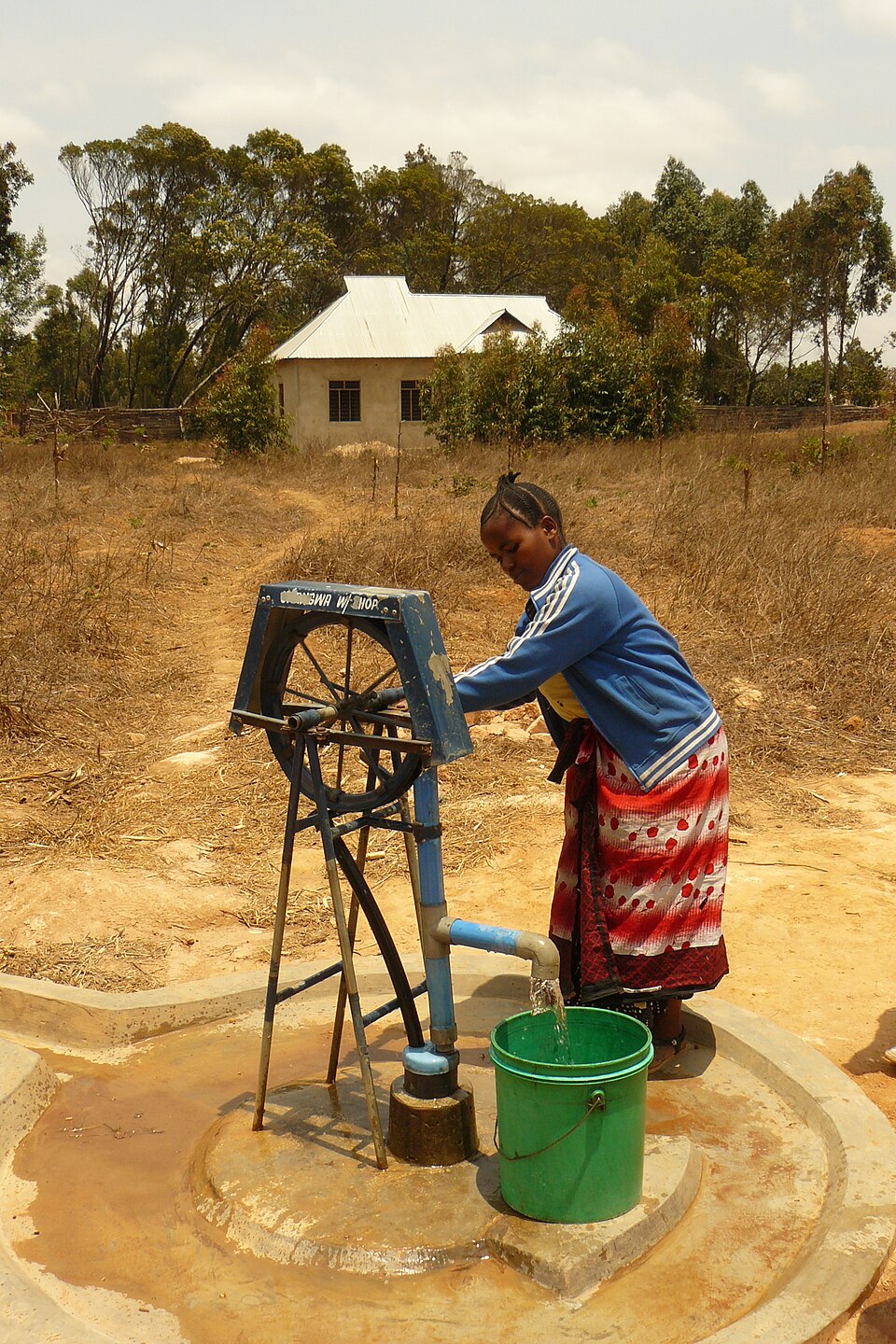 A rope pump over a sealed well in Tanzania. Turning the wheel draws washers on a rope up the pipe, lifting water with no bucket ever touching it.