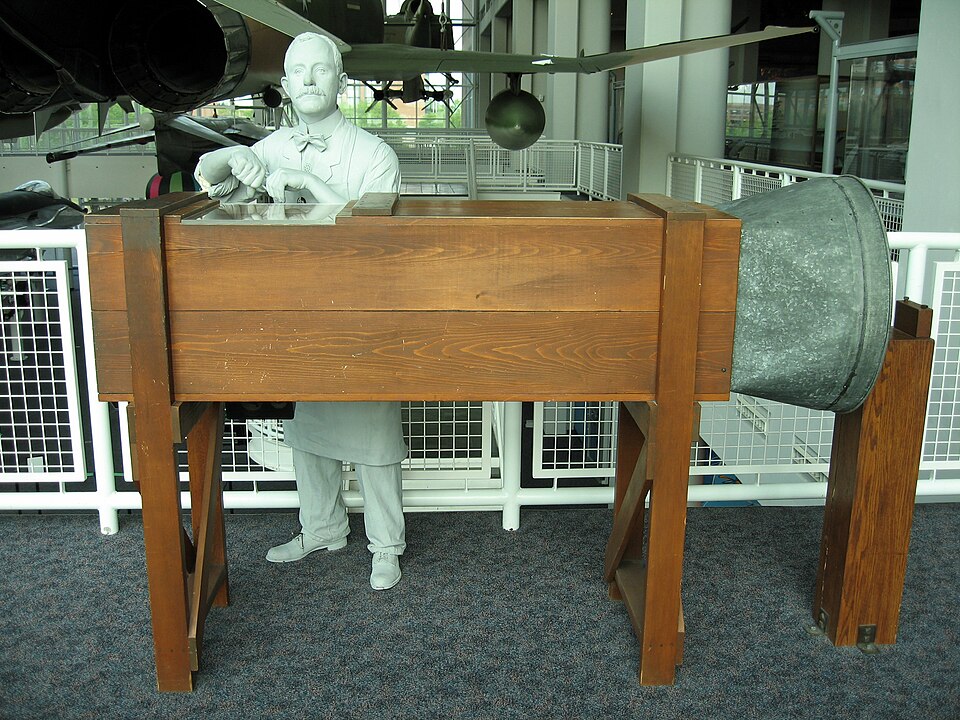 Another replica of the Wrights' wind tunnel, with a figure of one of the brothers at its viewing window.