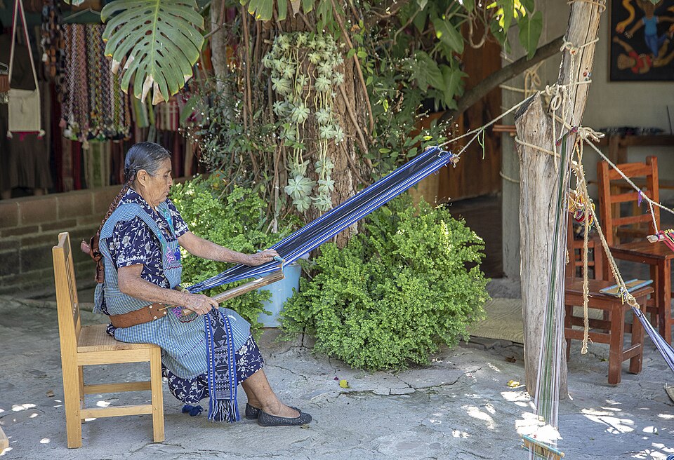 Weaving on a backstrap loom in Oaxaca: the far end tied to a post, the near end to a strap round the weaver, who leans back to tension the warp.